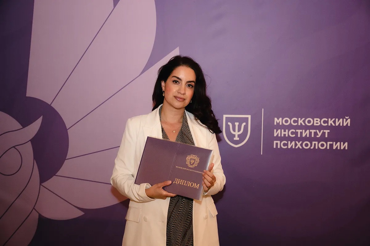 Выпускница с дипломом на фоне пресс-стены МИП